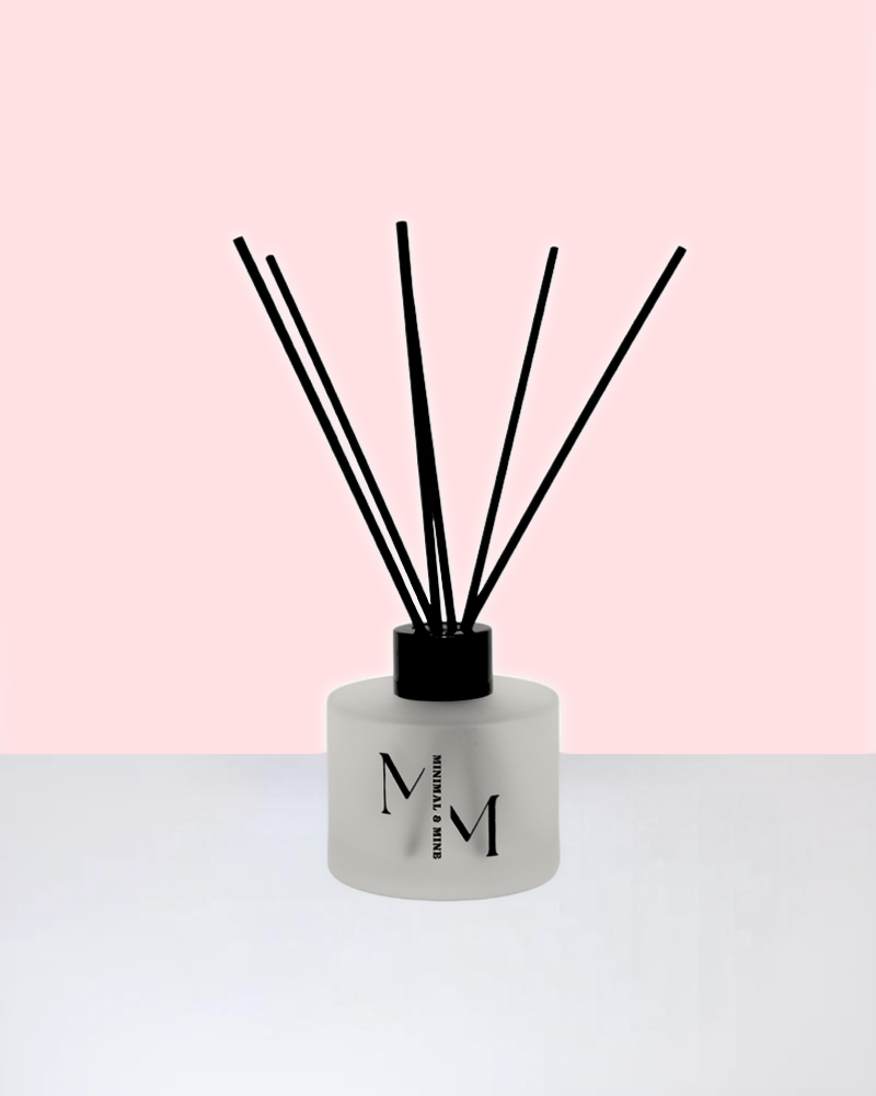 La FLEUR REED DIFFUSER displayed against a soft pink background with black reed sticks.