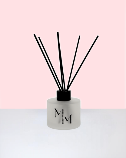 La FLEUR REED DIFFUSER displayed against a soft pink background with black reed sticks.