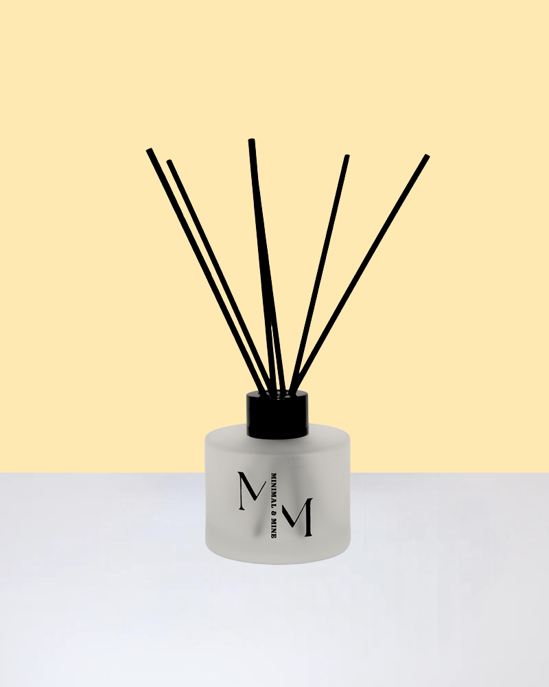 BEACH PLEASE REED DIFFUSER with black reeds in a stylish frosted glass bottle on a soft background.
