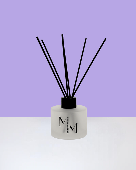 DOVES IN THE WIND REED DIFFUSER displayed against a purple background with black reeds.